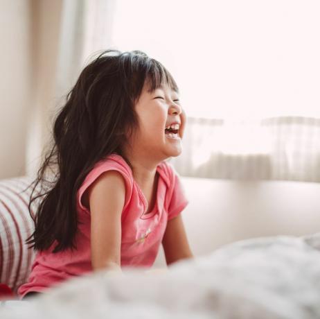 Väike tüdruk naerab voodis rõõmsalt