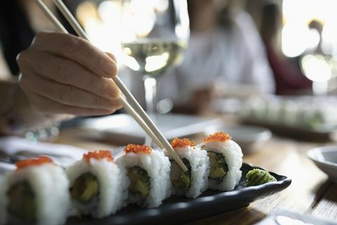 Naine söögipulgadega, mis ulatub restoranisalusele sushi järele