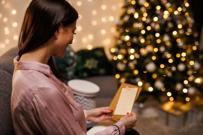 õnnelik noor naine istub diivanil, sätendava jõulupuu ääres, avab ja loeb kingitusega kaasa saadud jõulukaarti