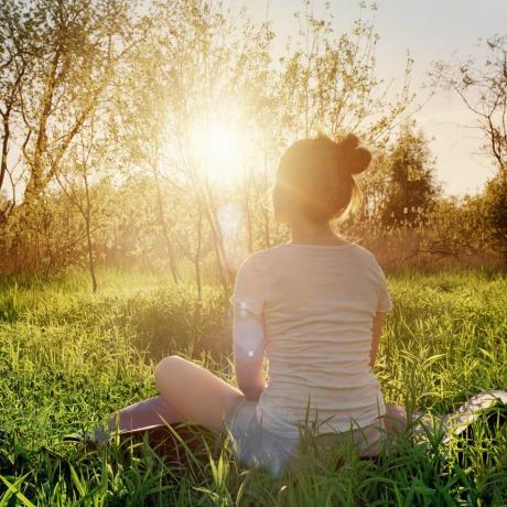 noor naine istub joogaasendis ja naudib looduses päikeseloojangut